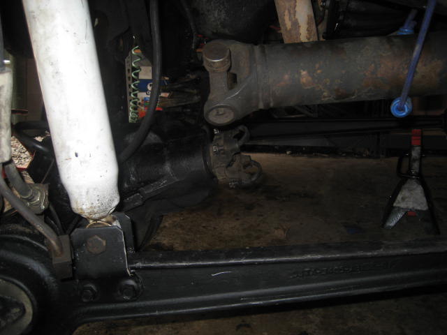 Close-up of a vehicle's rear axle, driveshaft, and shock absorber, with the vehicle supported by jack stands