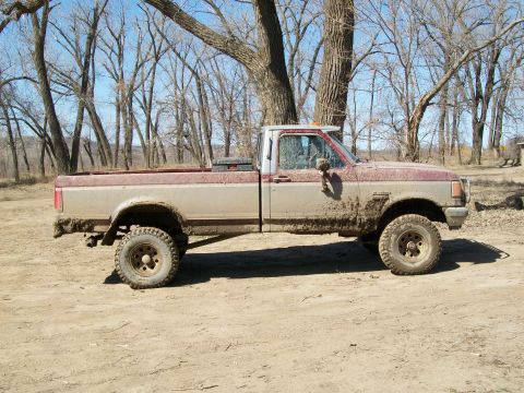 1988 Ford F-150 - Side view of a mud-splattered pickup truck parked on a dirt road under a clear sky.