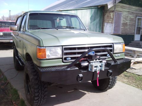 1989 Ford Bronco - A modified green Ford Bronco is parked in front of a building, with another vehicle visible behind it.