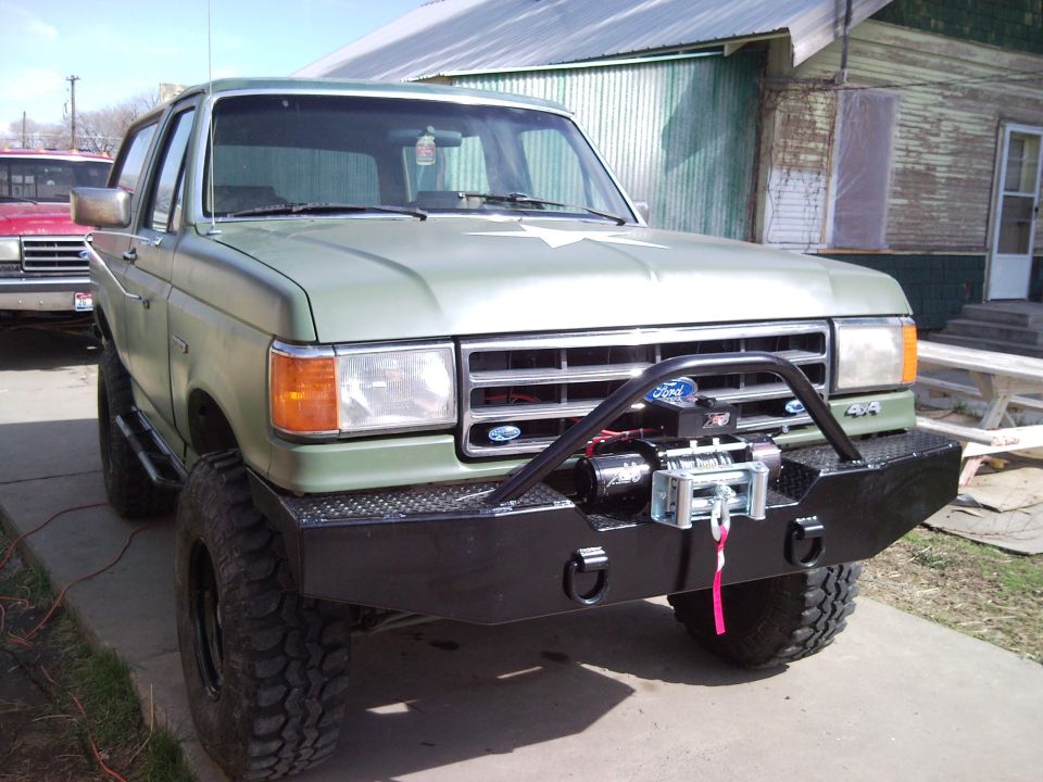 Green Ford Bronco with aftermarket bumper and winch. Another red Ford truck is parked behind it