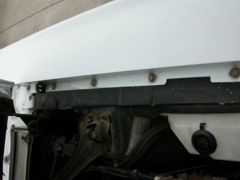 1968 Mercury Cougar - Close-up view of the radiator support area under the hood of a white vehicle, showing mounting hardware and black trim pieces.