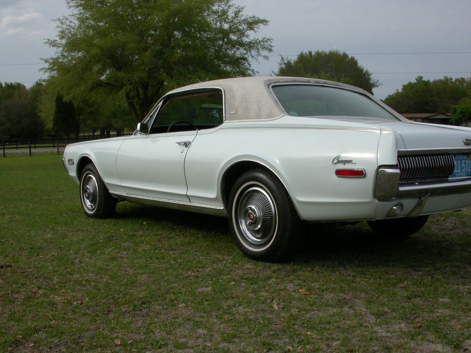 White 1968 Mercury Cougar parked on grass, showing rear quarter panel and grille. Vinyl top visible