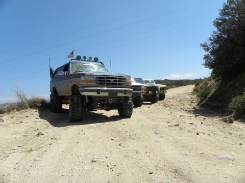 1995 Ford Bronco - Several modified Ford Broncos are lined up on a rough dirt trail under a clear blue sky.