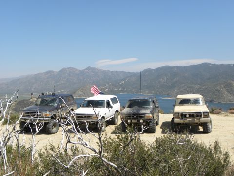 1995 Ford Bronco - A group of off-road vehicles are parked on a scenic overlook with a large body of water and mountains in the distance.