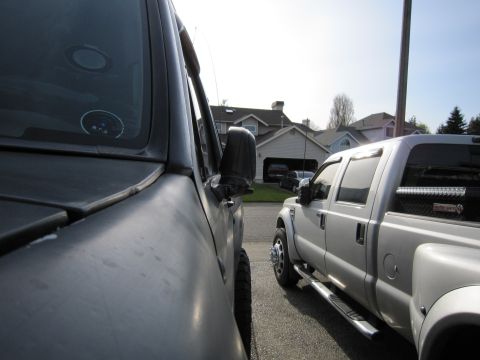1996 Ford Bronco - Two pickup trucks are parked side-by-side in a residential area with houses in the background.