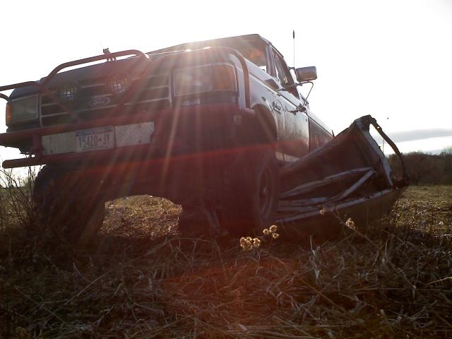 1995 Ford F-150 with custom front bumper and damaged bed, parked in a field