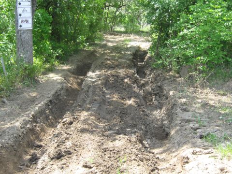 Muddy off-road trail with deep tire tracks and trail signs on a tree