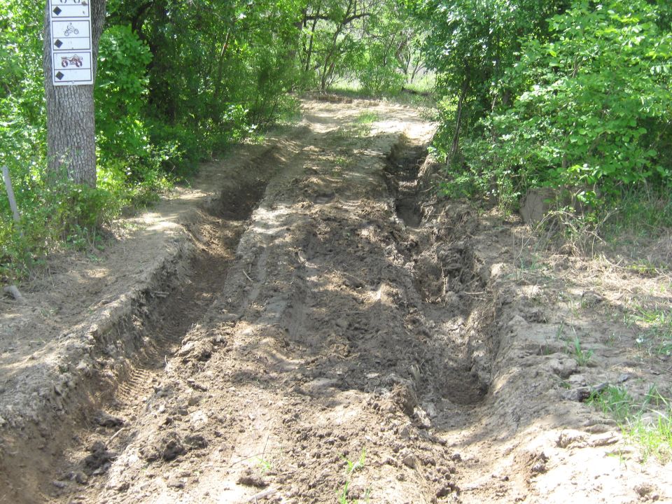 Muddy off-road trail with deep tire tracks and trail signs on a tree