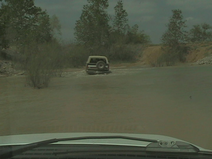 White 1990 Ford Bronco driving through water, rear view