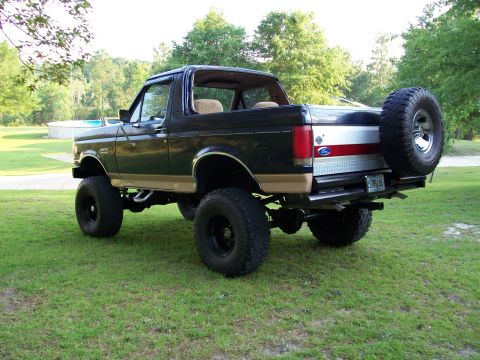 1990 Ford Bronco - This lifted 1990 Ford Bronco is parked on a grassy lawn with trees and a pool in the background.