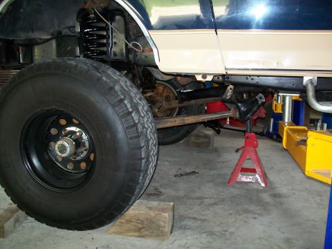 1990 Ford Bronco - Undercarriage of a 1990 Ford Bronco, showing suspension and large tire, supported by jack stands.
