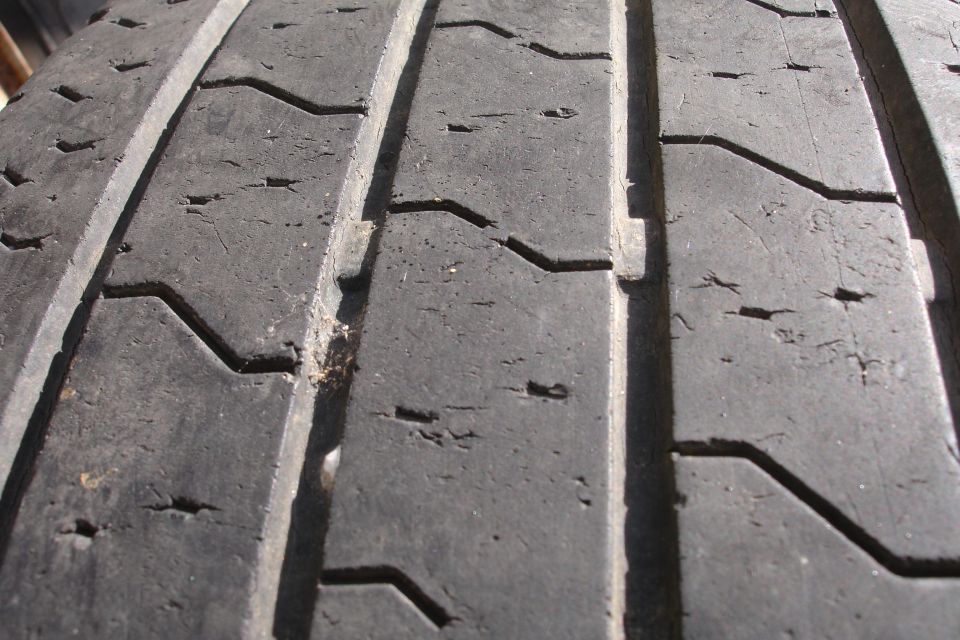 Close-up of a worn tire tread with visible cracks and debris