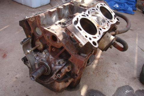 1989 Ford Taurus - A heavily rusted engine block sits on a concrete surface, with the cylinder head detached, revealing the pistons within.