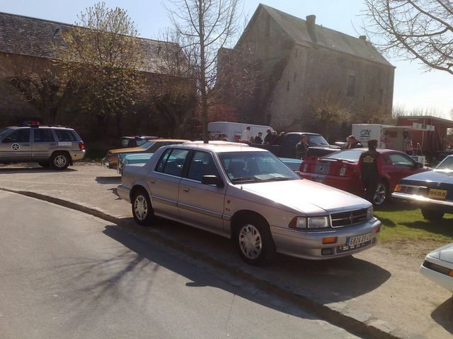 Silver sedan parked on a street, front 3/4 view. Visible details include alloy wheels and a license plate