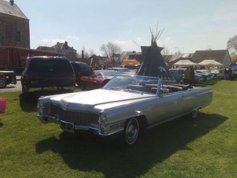1991 Ford Crown Victoria - A classic silver convertible is on display at an outdoor car show with other vehicles and tents in the background.