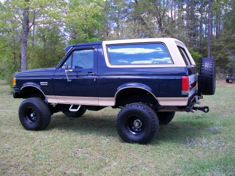 1990 Ford Bronco - This lifted Ford Bronco is shown from the side, with a spare tire on the back and large off-road tires.