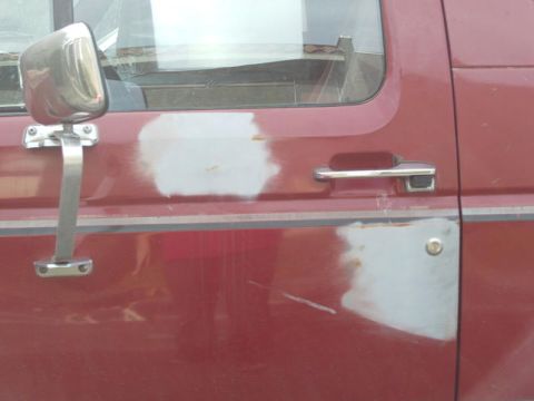 1988 Ford Bronco - Patches of body filler are visible on the red door of an SUV, near the side mirror and door handle.