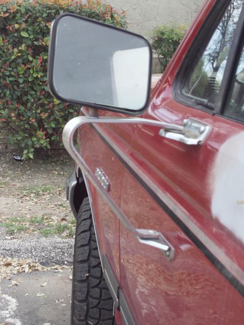 1988 Ford Bronco - Side view of a red truck door with chrome trim and a large side mirror, showing signs of repair.