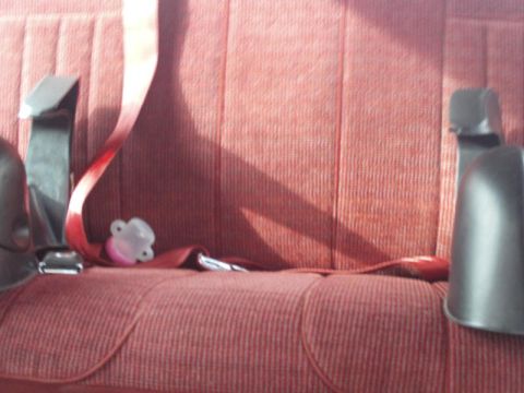 1988 Ford Bronco - A pacifier rests on the seatbelt buckle in the interior of a vehicle.