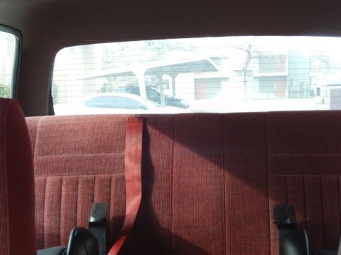 1988 Ford Bronco - View from the back seat shows a red velour bench seat and a glimpse of the outside world.
