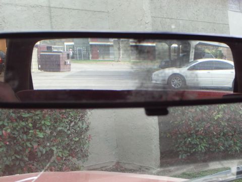 1988 Ford Bronco - View through the interior rear view mirror shows a white sedan and a brick structure in the background.
