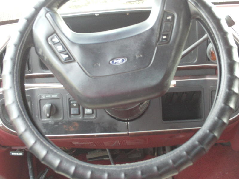 Steering wheel and dashboard of a red 1987 Ford Bronco, showing a Ford logo on the steering wheel
