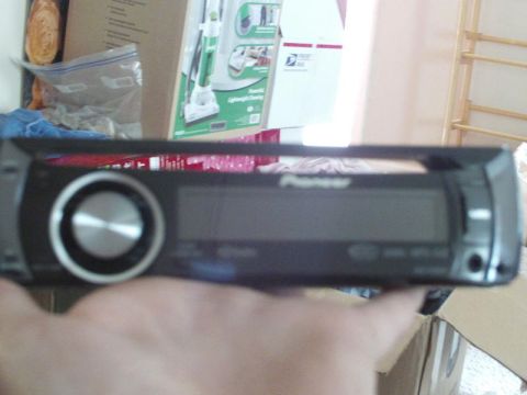 1988 Ford Bronco - A Pioneer car stereo is held in front of boxes. The device features a prominent silver knob and a digital display.