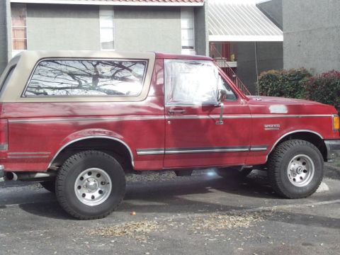 1988 Ford Bronco - Side profile of a red 1988 Ford Bronco with a tan top parked outdoors.