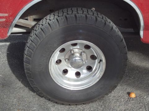 1988 Ford Bronco - A close-up view of a vehicle's tire and wheel assembly, with a small orange object on the asphalt.