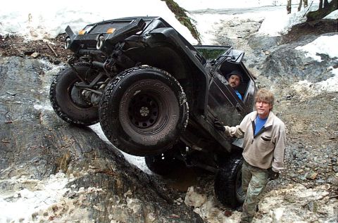 2002 Ford F-350 - A black off-road vehicle navigates a challenging rocky incline, with two individuals present near the vehicle.