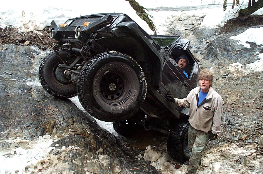 Black soft-top 4x4 flexed on a snowy rock ledge with a spotter at the fender