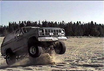 2002 Ford F-350 - SUV jumps over sand dune, with Supermotors.net logo in the foreground.