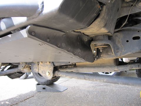 1996 Ford Bronco - Close-up view of the undercarriage and skid plate of a vehicle, with one wheel elevated on a ramp.