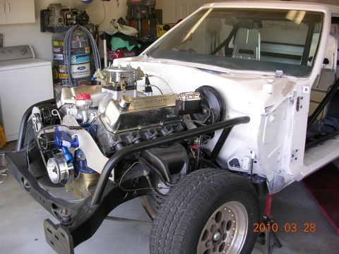1972 Ford Ranchero - The engine bay of a white vehicle is shown, a V8 engine, roll cage, and a racing seat inside the cabin.