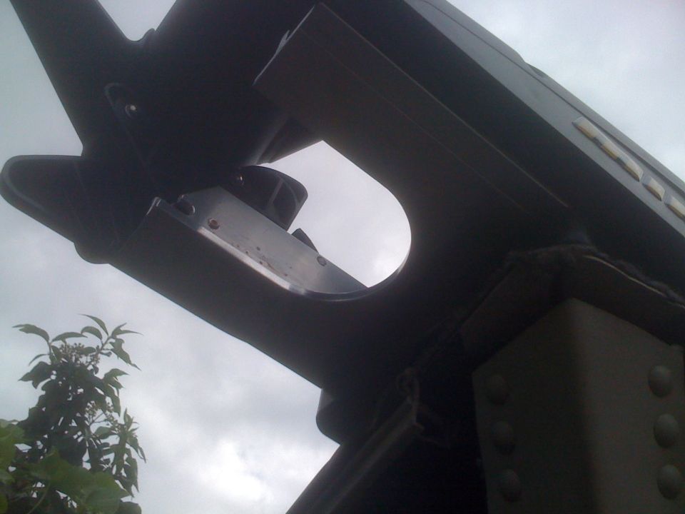 Dark metal structure with rivets and a circular cutout against a cloudy sky