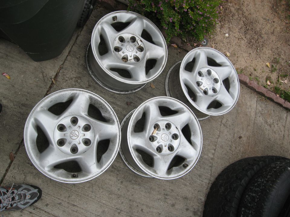 Four silver alloy wheels with five spokes and Toyota logos, resting on concrete