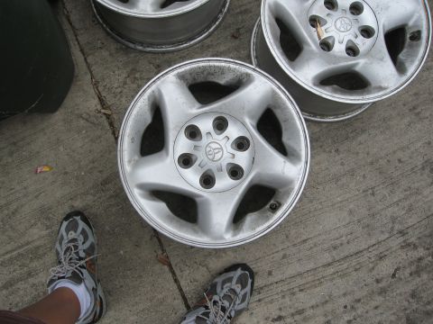 1986 Ford Bronco - Several five-lug wheels, likely from a Toyota, are shown resting on a concrete surface.