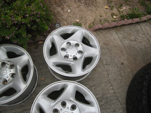 1986 Ford Bronco - A set of three silver alloy wheels, likely from a Toyota vehicle, are shown resting on a concrete surface.