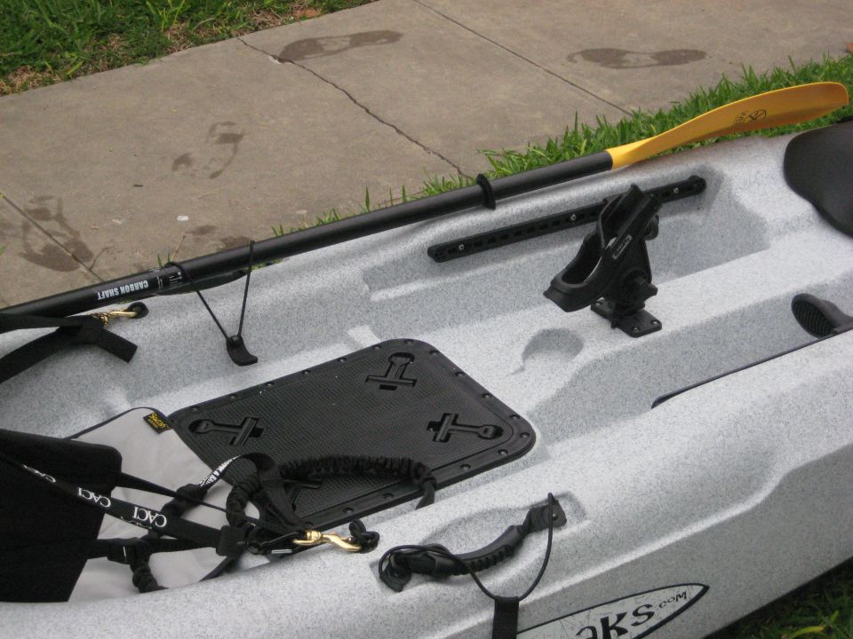 Light gray speckled kayak with black paddle, seat, and accessories on concrete