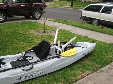 1953 Ford Mainline - A kayak equipped for fishing sits on a lawn, with a maroon SUV and a white station wagon parked on the street behind it.