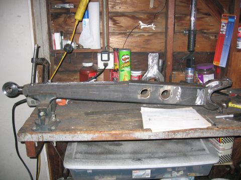 1989 Ford Bronco - A fabricated metal suspension component is secured in a vise on a workbench, surrounded by tools and supplies.