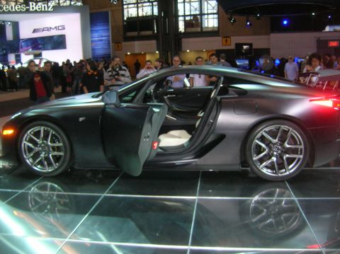 1996 Ford Bronco - A dark grey sports car with its doors open is displayed indoors.