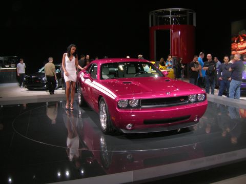 1996 Ford Bronco - A pink Dodge Challenger with white racing stripes is showcased on a display platform with a woman standing beside it.