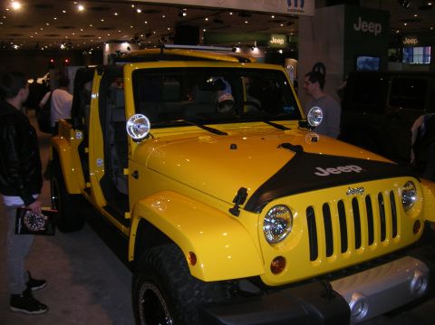 1996 Ford Bronco - A bright yellow Jeep Wrangler is displayed with its doors removed, a black decal on the hood and the Jeep logo visible.