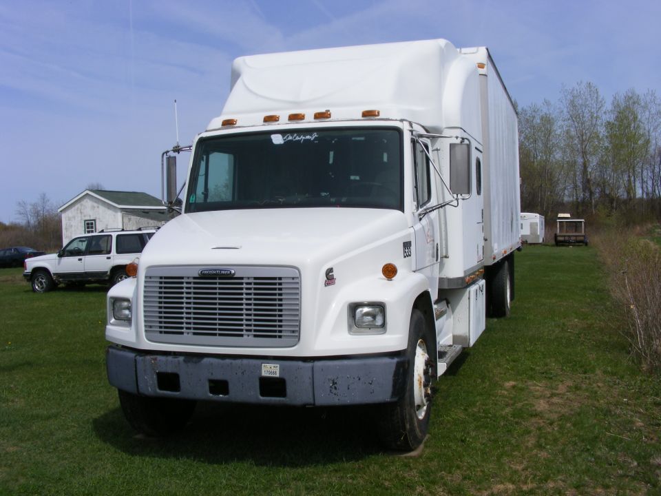 White Freightliner box truck with roof fairing and Cummins badge parked on grass