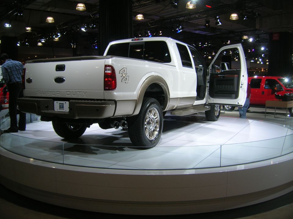 White Ford Super Duty pickup truck with driver's door open, on display. Red Ford pickup visible in background