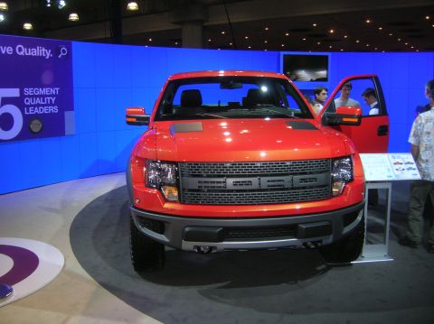 1996 Ford Bronco - An orange Ford F-150 Raptor truck is displayed with its driver's door open.
