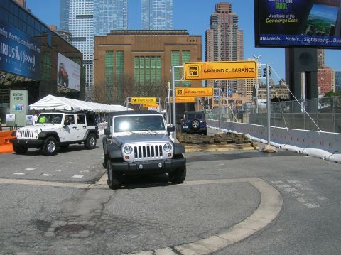 1996 Ford Bronco - Jeep Wranglers navigate an obstacle course with city buildings in the background.