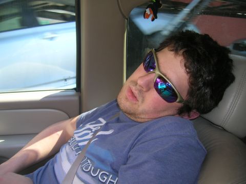 1996 Ford Bronco - A man wearing sunglasses and a blue t-shirt is asleep in the passenger seat of a vehicle.