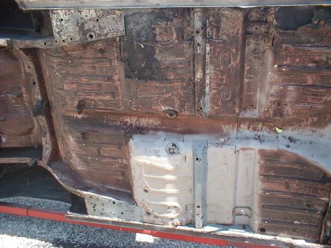1964 Ford Fairlane - The undercarriage of a vehicle displays significant rust and wear on its floor pans and structural components.